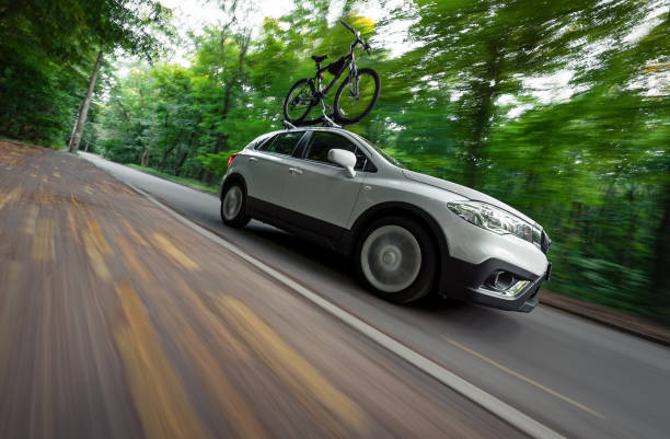 Suzuki SX-4 driving in a green forest with a bicycle on a roof rack. Low angle view of the right side. Kyiv, Ukraine - August 07 2019.