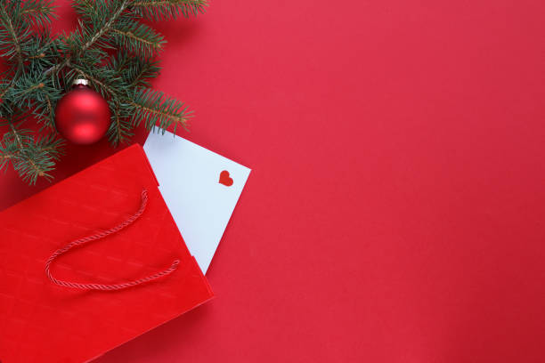 A Christmas-themed composition featuring a red gift bag and a red ornament. The items are arranged on a vibrant red background, complemented by a pine branch to add a festive touch.