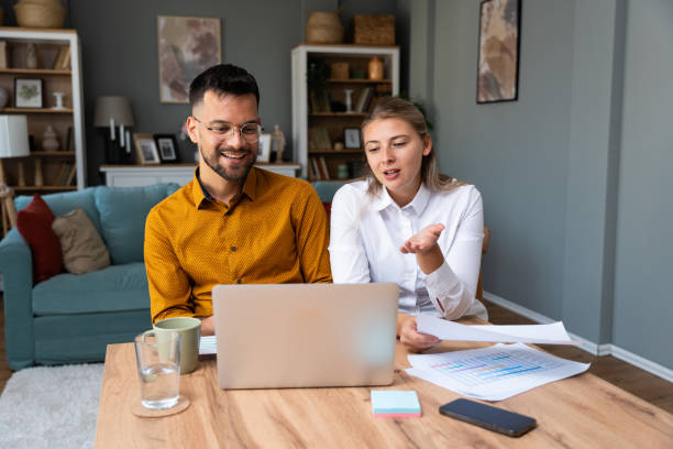 istock Working at home. Young freelance couple work from home office on laptop computer having video call with clients, showing statistics of business improvement with sales graphic printed on paper. 2171682255