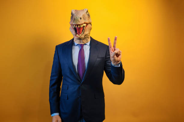 istock A man wearing a dinosaur mask showing two fingers on yellow background. 2171692585