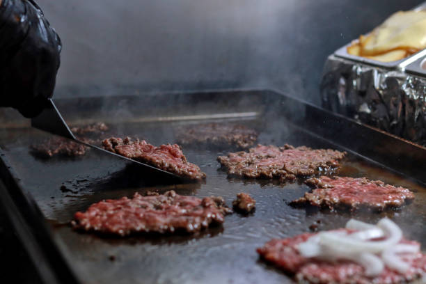 Smash burgers being prepared on a griddle with onions, showing the sizzling cooking process Smash burgers being prepared on a griddle with onions, showing the sizzling cooking process in a professional kitchen spanish hamburger stock pictures, royalty-free photos & images