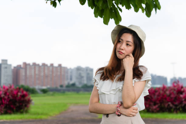 Wearing a light, summery outfit consisting of a white blouse, beige skirt, and a white sun hat. Sunny, cloudy, summer season.