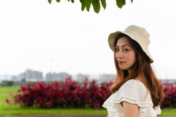 Wearing a light, summery outfit consisting of a white blouse, beige skirt, and a white sun hat. Sunny, cloudy, summer season.