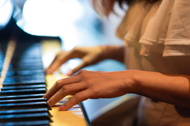 Wearing a light, summery outfit consisting of a white blouse, beige skirt, and a white sun hat. Black piano, playing