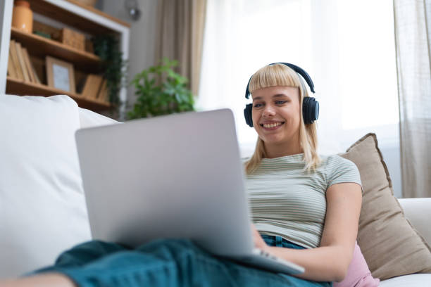 istock Young happy freelance worker or university student woman sitting work at home on sofa working on laptop, while listening podcast or listen the music, favorite song, enjoying freedom and independence. 2171694595