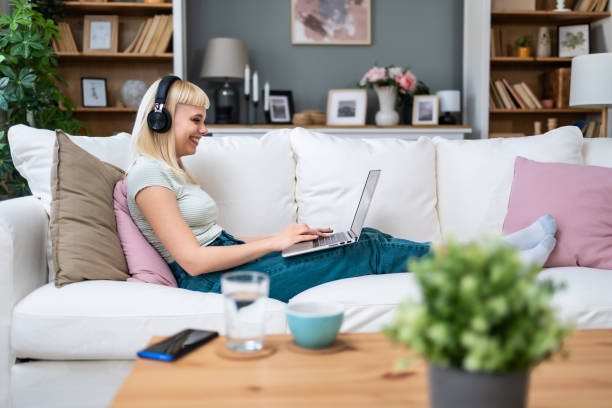 istock Young happy freelance worker or university student woman sitting work at home on sofa working on laptop, while listening podcast or listen the music, favorite song, enjoying freedom and independence. 2171694608