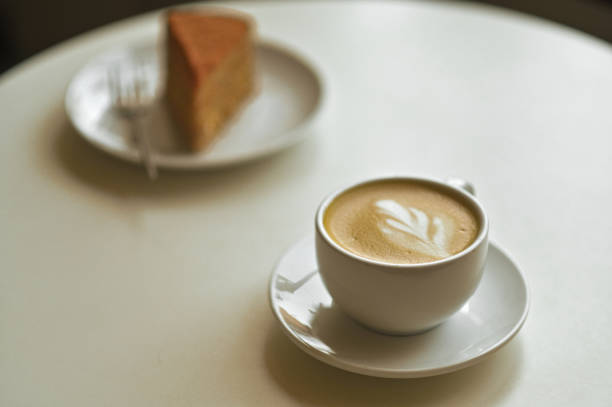 a cup of cappuccino latte with latte art and cake on the table.