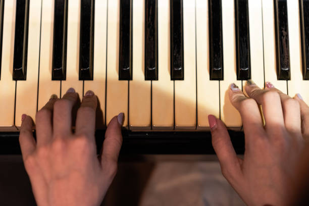 Wearing a light, summery outfit consisting of a white blouse, beige skirt, and a white sun hat. Black piano, playing