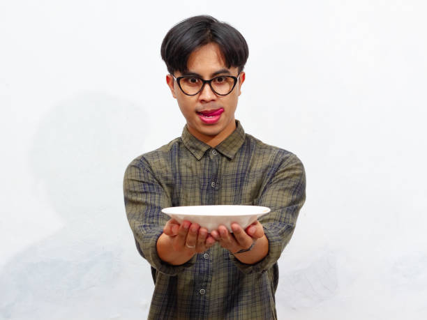 istock A handsome young Asian man excitedly looking at an empty plate with a happy expression, isolated on a white background. Perfect for food or advertisement concepts. 2171699954