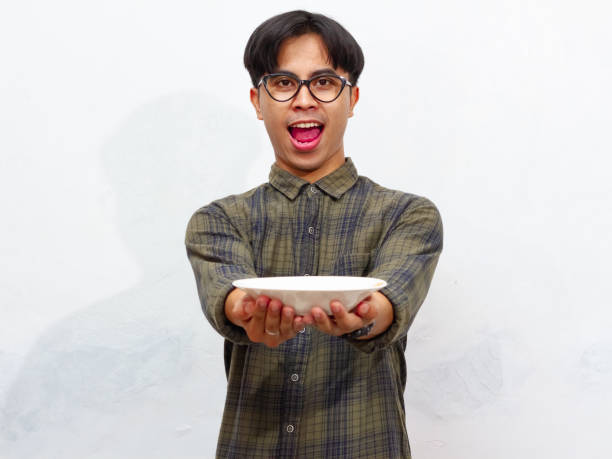 istock A handsome young Asian man excitedly looking at an empty plate with a happy expression, isolated on a white background. Perfect for food or advertisement concepts. 2171700026