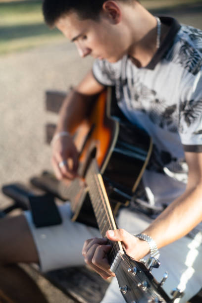 Young man learning to play guitar from internet lessons on a mobile phone in the park.