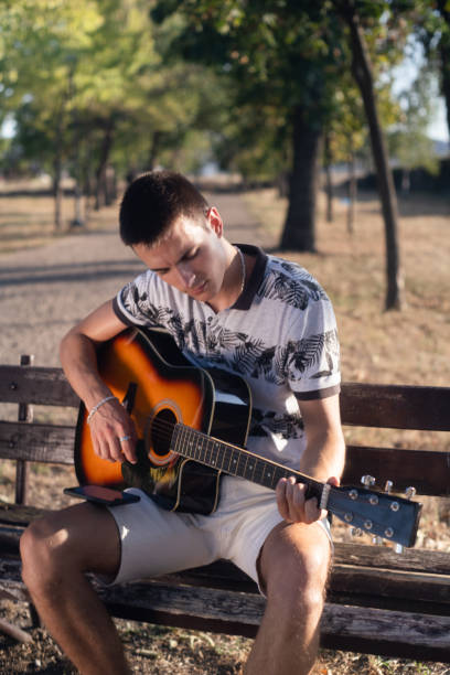 istock Young man on the park bench playing guitar on a sunny day 2171700449