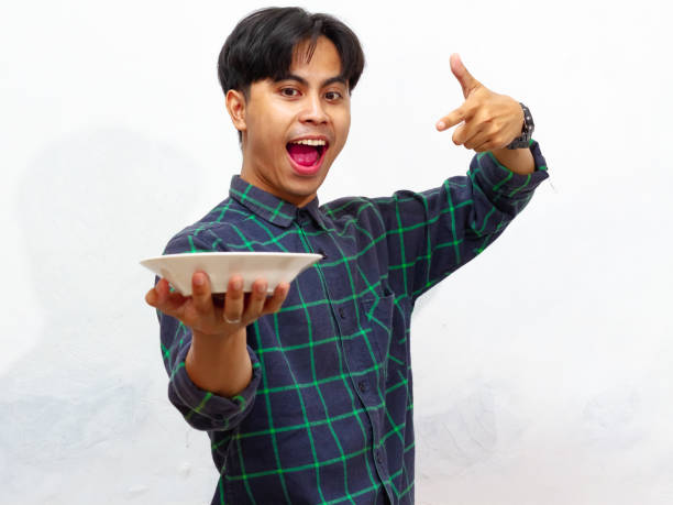 istock Handsome young Asian man pointing at an empty plate with an excited and happy expression, isolated on a white background. 2171700450