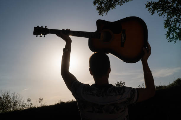 istock Man silhouette holding a guitar against sunny sky 2171700465