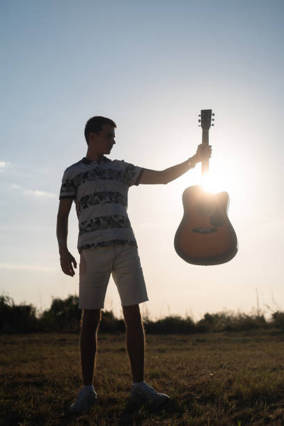 istock Man silhouette holding a guitar against sunny sky 2171700507