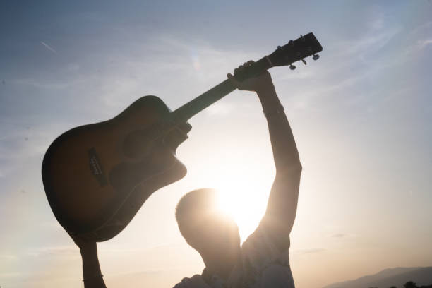 istock Man silhouette holding a guitar against sunny sky 2171700574
