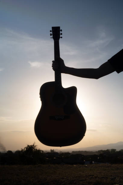 istock Man hand silhouette holding a guitar against sunny sky 2171700582