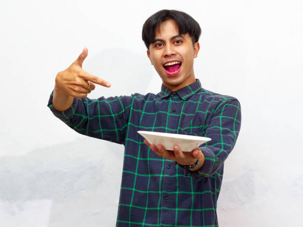 istock Handsome young Asian man pointing at an empty plate with an excited and happy expression, isolated on a white background. 2171700596