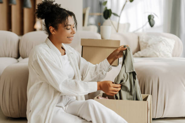 istock Young woman unpacking clothes from cardboard box at home 2171700945