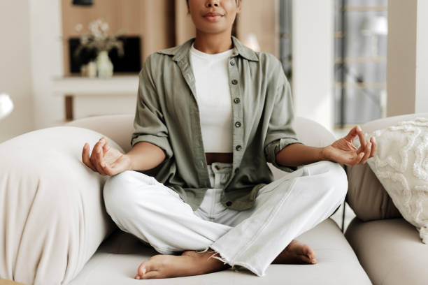 istock Young woman practicing yoga meditation at home sitting on sofa 2171701283