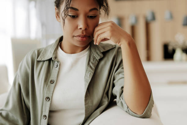 young woman feeling sad while sitting on sofa at home - megbánás témájú stock jellegű vizuális alkotások, jogdíjmentes fotók és képek