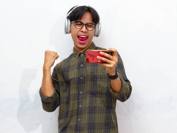 istock Excited happy young asian man gamer player using smartphone playing game in mobile videogame app or watching digital video stream holding cell phone isolated on white background. 2171702017