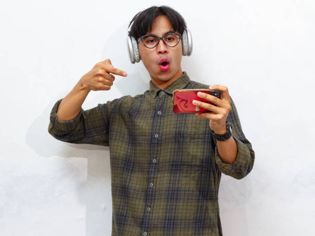 istock Excited happy young asian man gamer player using smartphone playing game in mobile videogame app or watching digital video stream holding cell phone isolated on white background. 2171702018