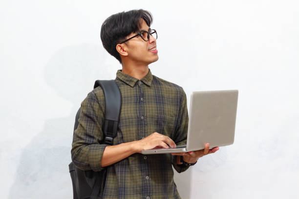 istock Smiling confident Handsome Asian male student carrying a backpack and holding a laptop, isolated on a white background, perfect for advertising. 2171705724