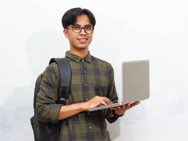 istock Smiling confident Handsome Asian male student carrying a backpack and holding a laptop, isolated on a white background, perfect for advertising. 2171705947