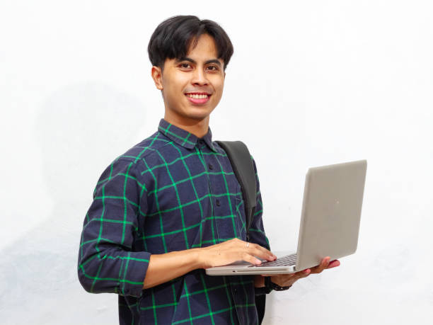 istock Smiling confident Handsome Asian male student carrying a backpack and holding a laptop, isolated on a white background, perfect for advertising. 2171706079