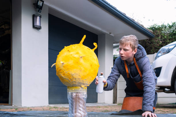 A young boy uses a can of yellow spray paint to color his model of the sun for his school science project.