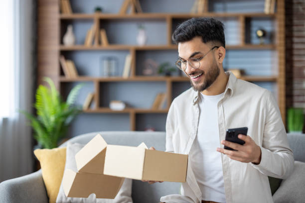 istock Young man excitedly opening a cardboard box while checking his smartphone at home 2171721747