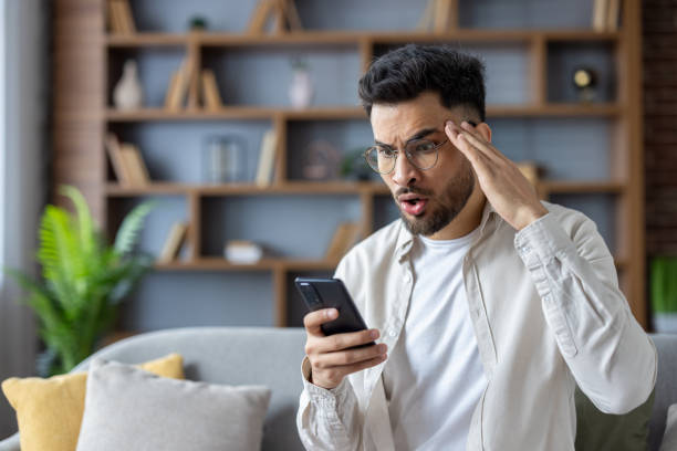 istock Shocked man looking at smartphone screen while sitting on couch at home 2171721826