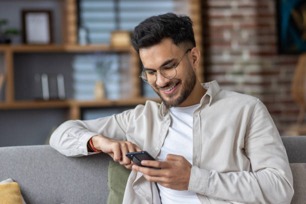 istock Smiling man using smartphone while relaxing on couch at home, enjoying digital content and staying connected 2171723858