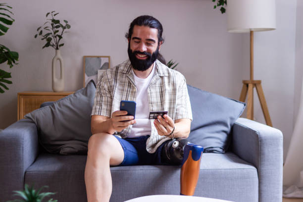 istock Smiling young man with prosthetic leg using smartphone for online shopping at home 2171723955