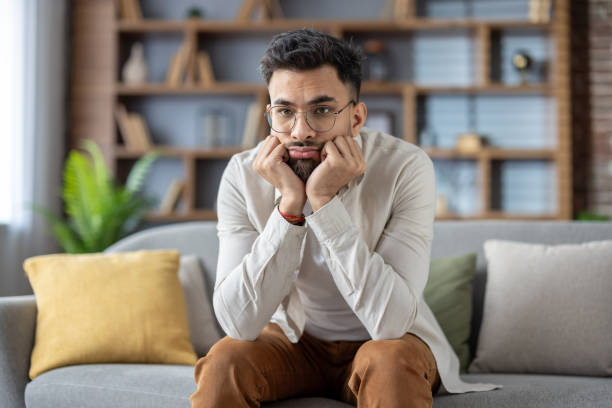 istock Thoughtful young man sitting on a sofa, reflecting on life decisions, wearing glasses and casual attire, conveying a sense of contemplation and introspection in a comfortable home setting 2171735257