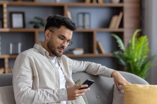 istock Relaxed man sitting on sofa using smartphone, browsing internet or checking social media in cozy living room with modern decor 2171735298