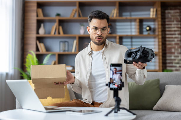 istock Man reviewing virtual reality headset at home workspace while recording video content on smartphone 2171736365