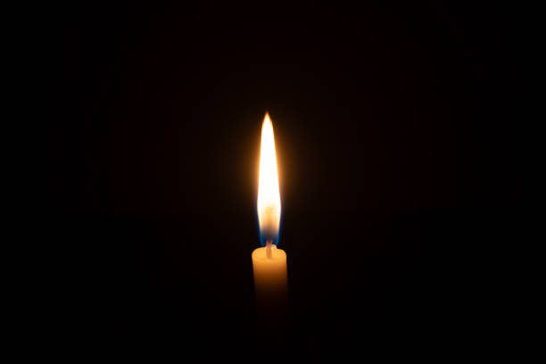 istock A single burning candle flame or light glowing on a small orange candle on black or dark background on table in church for Christmas, funeral or memorial service with copy space 2171738939