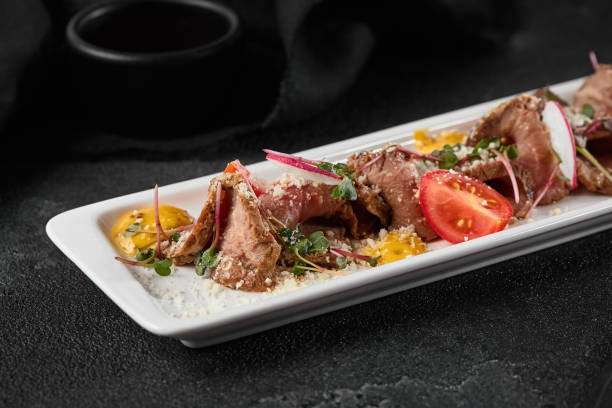 Gourmet Beef Roast with Fresh Vegetables on Elegant White Plate Against Dark Background