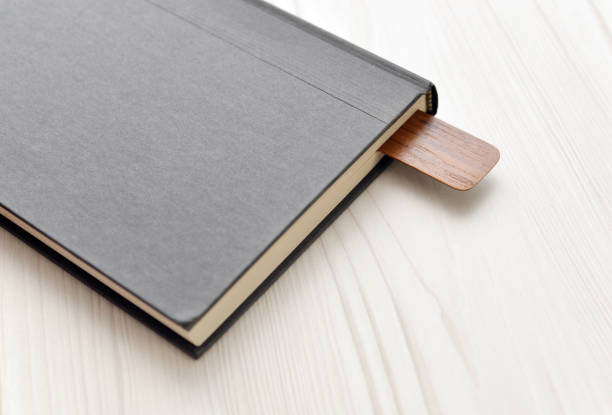 Closeup of a wood bookmark in a hard cover book on a whitewashed wood desk.