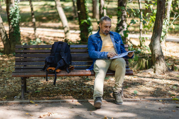 istock Man sits absorbed reading papers on park bench 2171760560