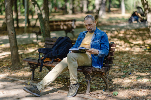 istock Man with a book and backpack relaxing on park bench. 2171760571