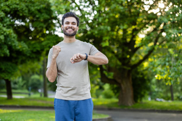 istock Smiling athlete tracks fitness progress on smartwatch while standing outdoors in a park surrounded by green trees 2171765250