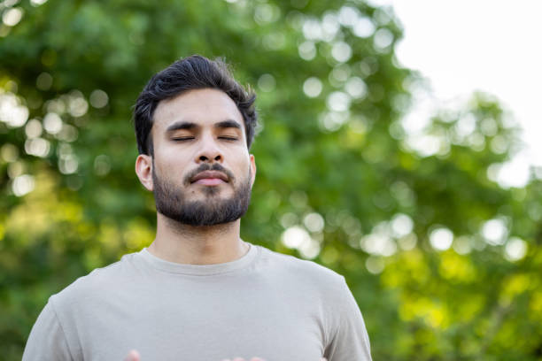 istock Young man practicing mindfulness and relaxation in outdoor nature setting with eyes closed, focusing on breathing techniques 2171766070