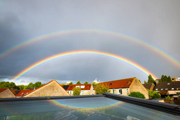 Bright colorful double rainbow over a residential area in the Netherlands. Part of the rainbow is reflected in a skylight.