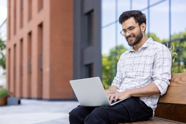 istock Smiling man working on laptop outdoors, sitting on bench in urban environment 2171768826