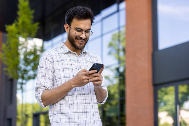 istock Happy young Indian male student standing outside university campus and using mobile phone 2171768837