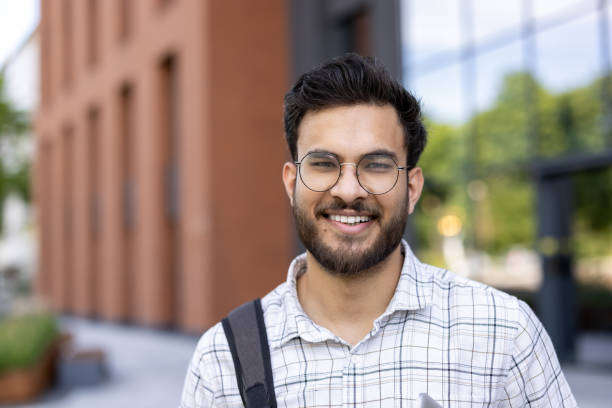 istock Smiling young man with glasses and beard holding phone outside modern building 2171768885