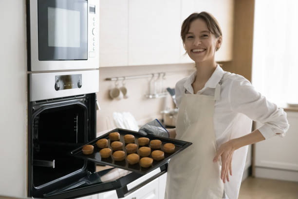 istock Young housewife in apron holding baking tray with cupcakes 2171770826
